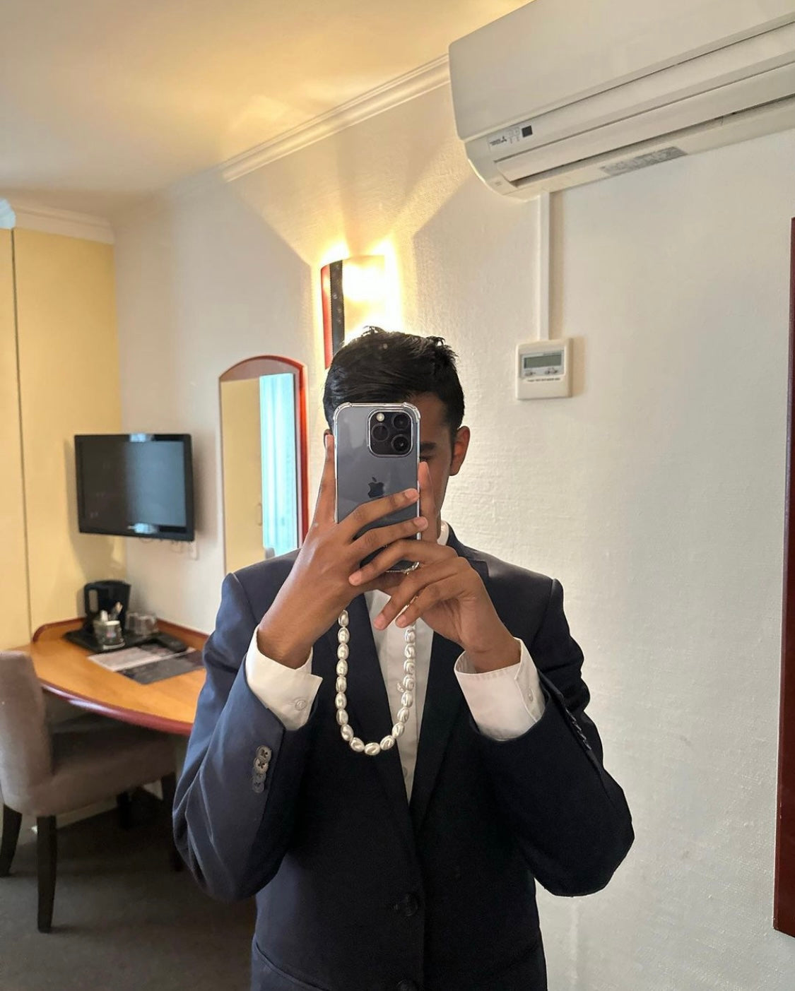 Person taking a mirror selfie in a room with a pearl-style phone case strap with gold clasps, elegant and detachable for a chic upgrade to any phone case or bag.